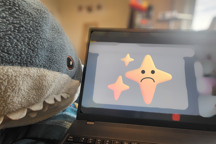 An IKEA BLĂ
HAJ next to a laptop computer, on which a piece of blurred software is open with the "sparkles" emoji that's been co-opted to represent AI functionality. The emoji has a sad face superimposed over the middle of the largest sparkle.